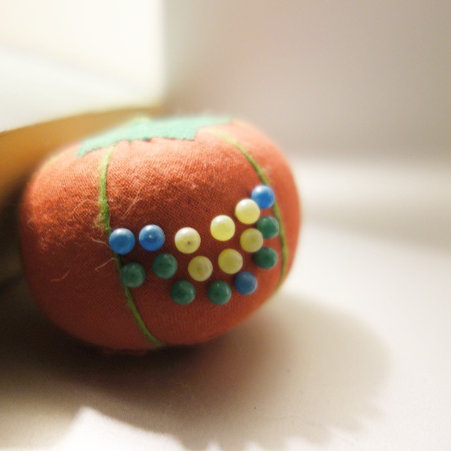 43: Colourful pushpins in the shape of a teacup, lodged in a red pincushion