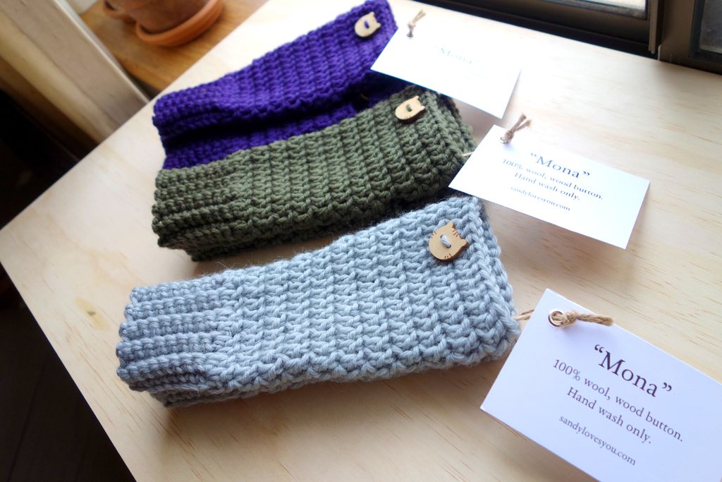Purple, olive green and sky blue pairs of fingerless gloves adorned with a wooden cat head button